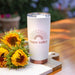 White Stocky Tumbler with copper base printed with Sunshine 'Napa Valley' branding next to sunflowers on a wooden table outdoors.